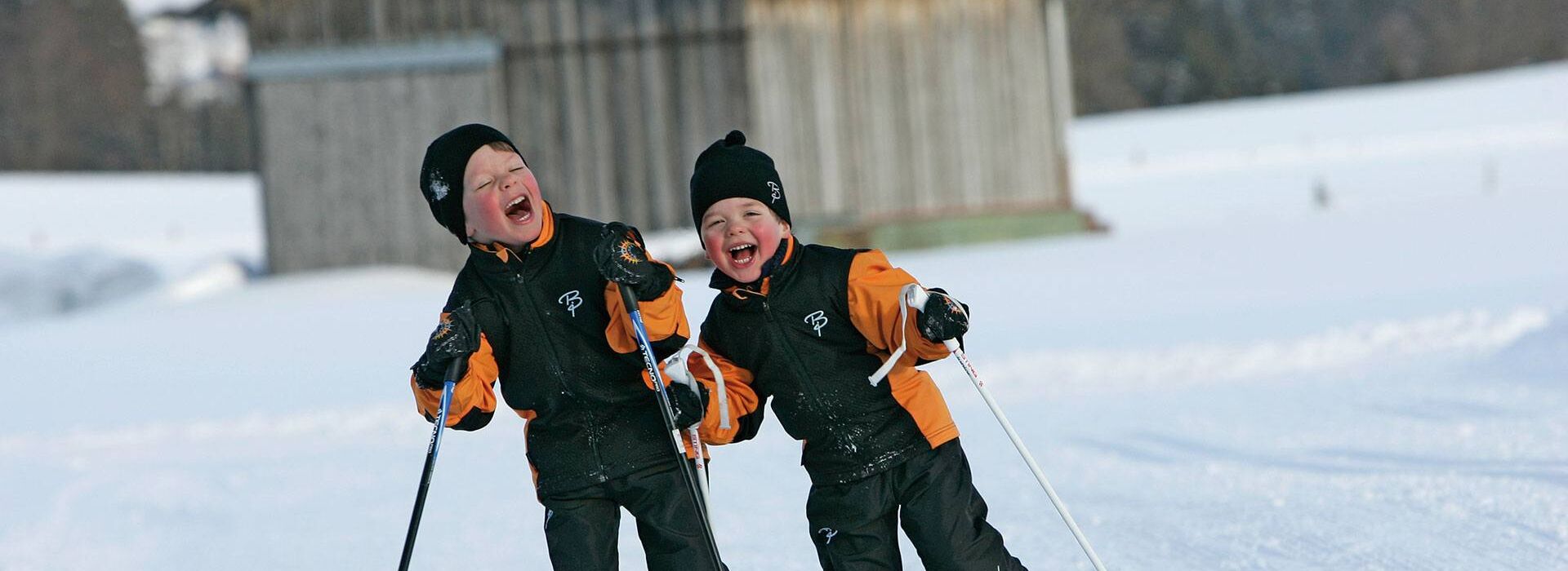 Two children cross-country skiing in orange and black jackets on a winter's day