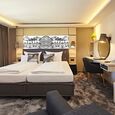 The double box-spring bed in a hotel room with a desk and plenty of natural light