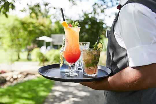 A waiter with a tray of cocktails, tonic water and other drinks in the garden