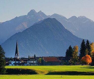 View of Fischen with a few houses and the church as well as the Allgäu Alps in the hazy background