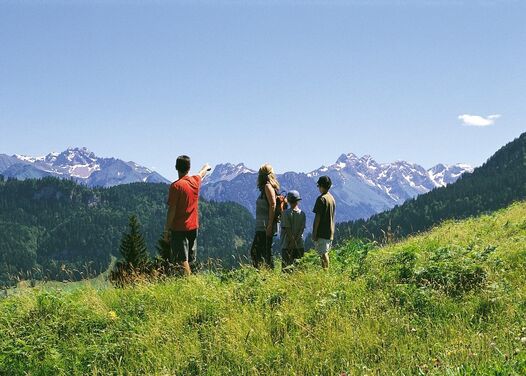 Parents with two children hiking at altitude looking at the mountain panorama in the distance