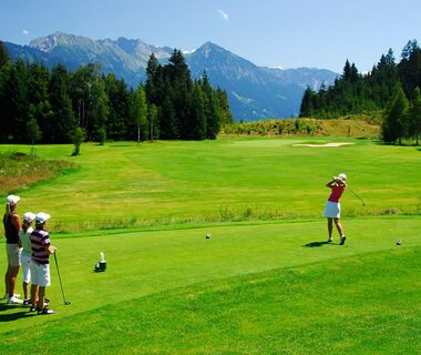 Four golfers at a tee on the Sonnenalp golf course with the Rubihorn in the background