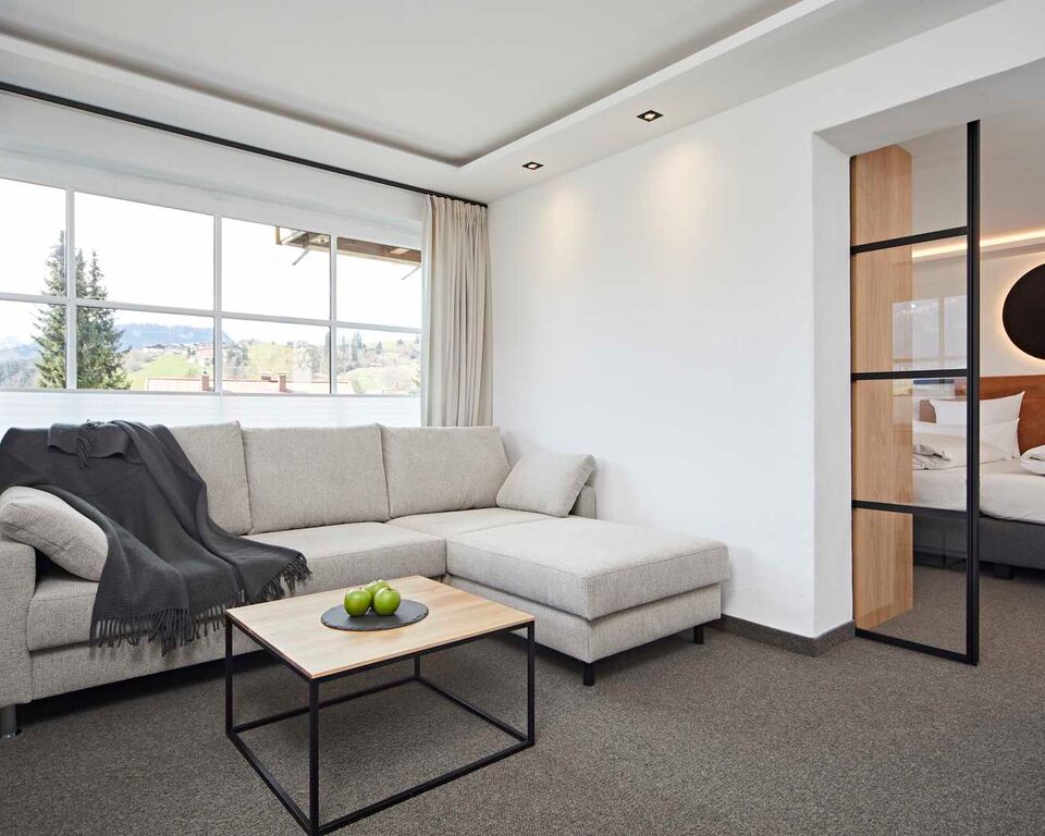 Wohnbereich mit Sofa und Wolldecke darüber in einem Hotelzimmer mit dem Schlafbereich im Hintergrund