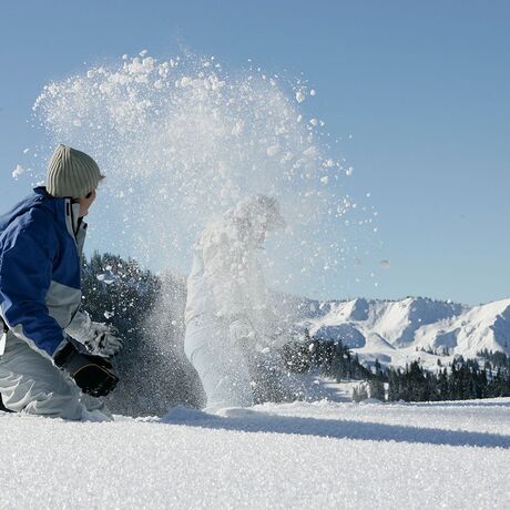 Zwei Personen spielen im frischen Schnee und werfen sich gegenseitig mit Schnee ab