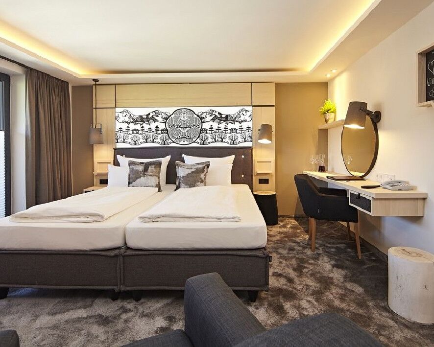 Das Doppel-Boxspringbett in einem Hotelzimmer mit Schreibtisch und viel Tageslicht