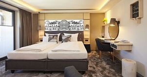 The double box-spring bed in a hotel room with a desk and plenty of natural light