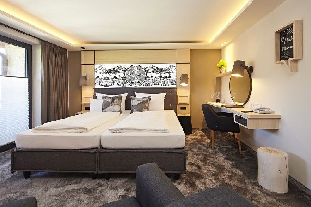 The double box-spring bed in a hotel room with a desk and plenty of natural light