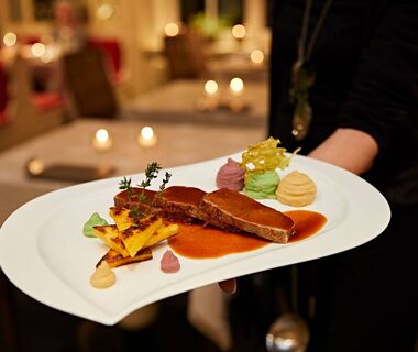 A waitress holds a beautifully presented meat dish