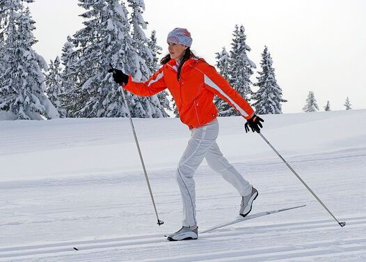 A woman in an orange jacket cross-country skiing in a snowy winter landscape