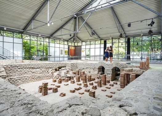 Two women stand in front of an excavation and consult with each other
