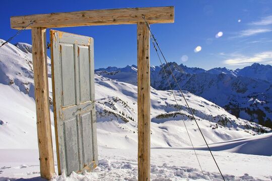 A door with a wooden door frame leading to nowhere with the Allgäu mountain panorama in the background