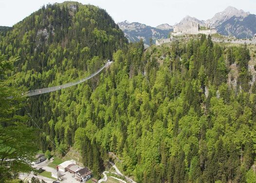 A suspension bridge spanning a valley with a ruined castle on the other side of the valley on the mountain