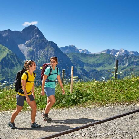 Zwei weibliche Wanderinnen auf einem Wanderweg in hoher Höhe mit den allgäuer Alpen im Hintergrund